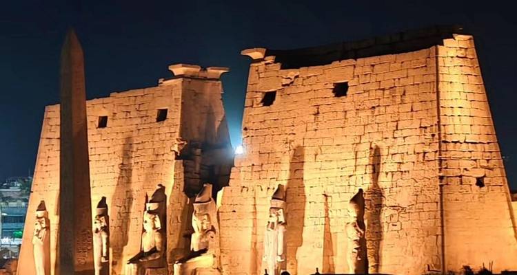 Vue nocturne des pylônes et des statues du temple de Louxor, chaleureusement illuminés contre le ciel sombre.