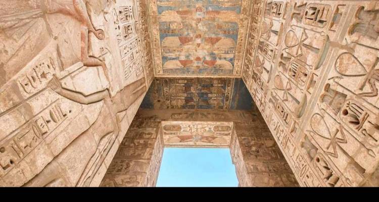 Vue ascendante d'une porte de temple révélant des plafonds couverts de hiéroglyphes colorés et une parcelle de ciel bleu.