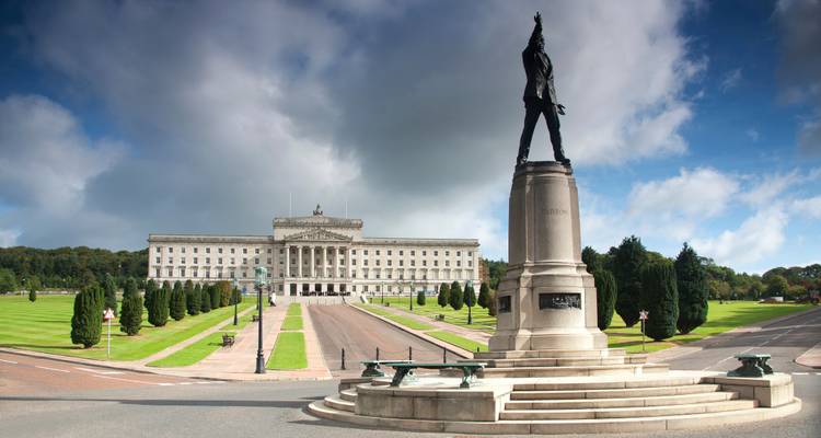 Bâtiments du Parlement de Stormont avec statue de bronze héroïque et pelouses impeccablement entretenues sous des nuages menaçants.