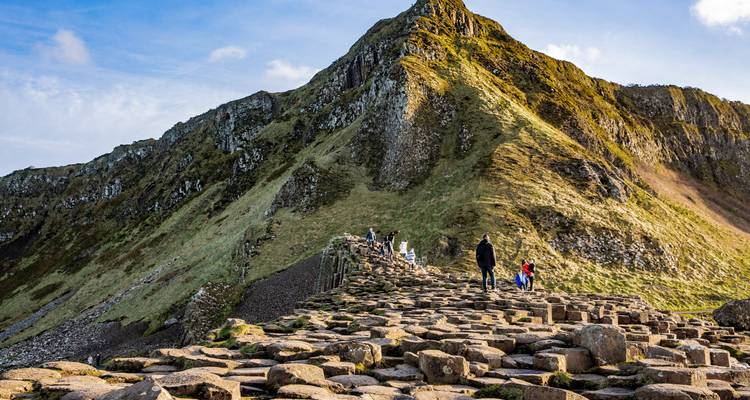 Visitors hike over the hexagonal basalt columns toward a rugged peak at Giant's Causeway.
