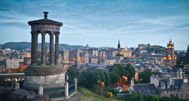 Dugald Stewart Monument overlooking the twinkling evening lights of Edinburgh cityscape.
