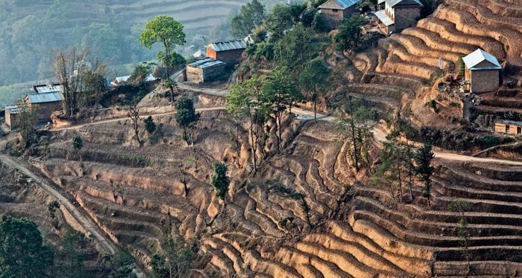 Aerial view of terraced farmland and scattered houses on a Nepalese hillside.