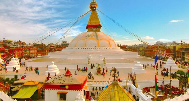 Panoramic view of Boudhanath Stupa with bustling pilgrims and colourful prayer flags.