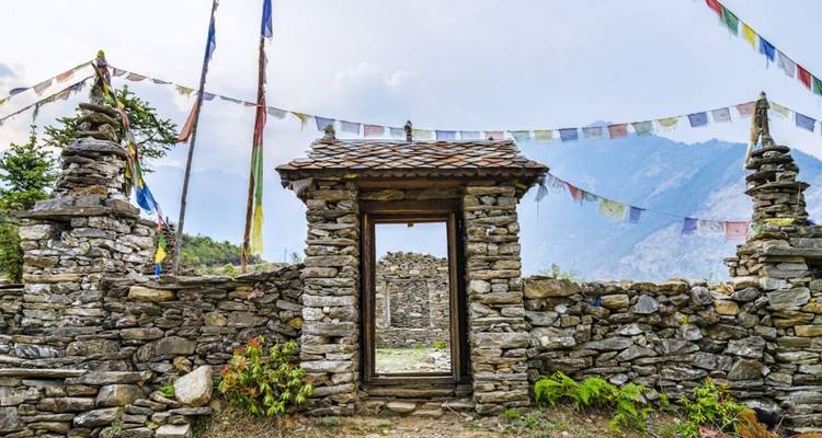 Stone gate and cairns adorned with prayer flags overlooking misty mountain ridges.