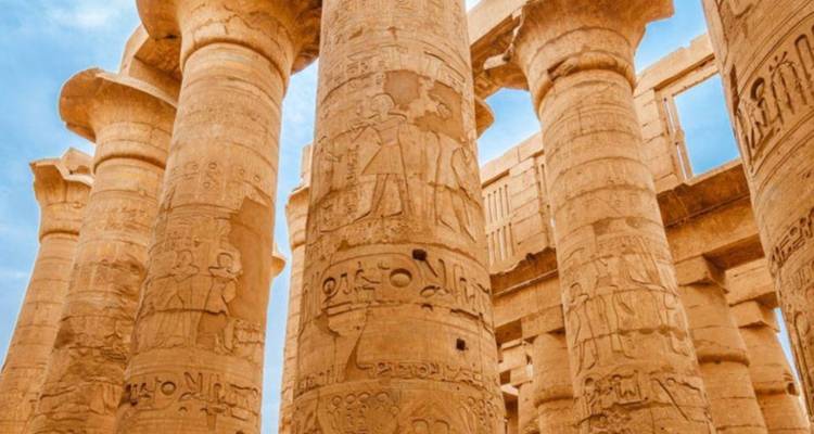 Impressive sandstone columns of Karnak covered in detailed hieroglyphic carvings under blue sky