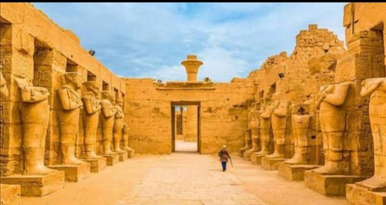Long corridor flanked by standing sandstone statues leading to an open doorway of an ancient temple