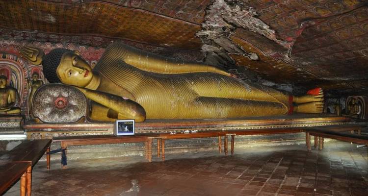 Large reclining Buddha statue inside dimly lit cave temple adorned with ancient paintings.