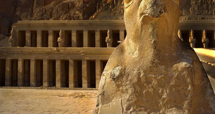 Close-up of a falcon-headed statue with the terraced Temple of Hatshepsut in the background