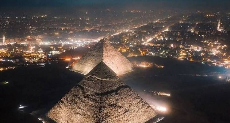 Night aerial view of illuminated pyramids with the sprawling city lights of Cairo beyond