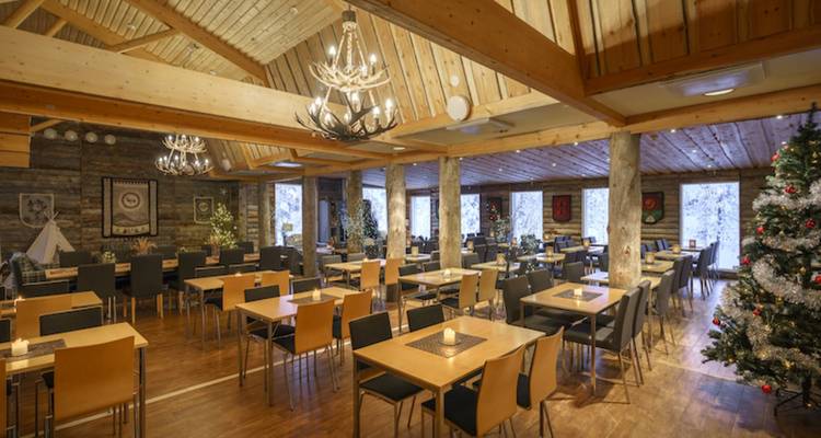 Spacious wooden restaurant hall with chandeliers, set for group dining in a winter lodge.