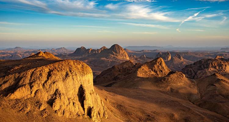 Sweeping view of rugged desert mountains glowing in warm late-day light beneath a vivid sky