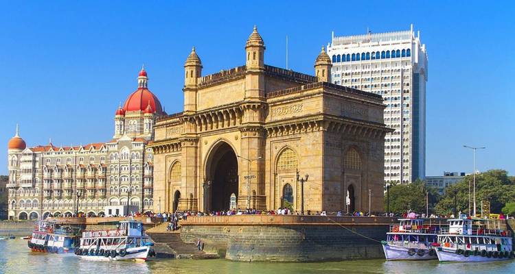 Iconic Gateway of India with boats and tourists against a bright blue Mumbai sky.
