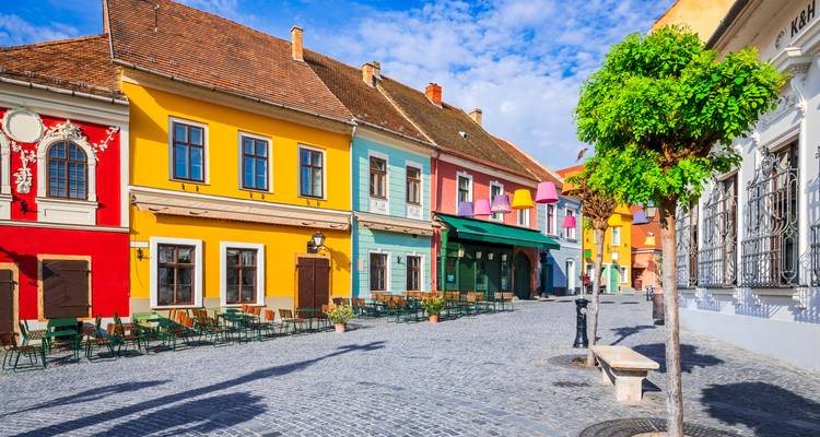 Las fachadas barrocas de colores vivos y las mesas de cafés al aire libre bordean una calle empedrada bajo un cielo azul radiante en Szentendre.