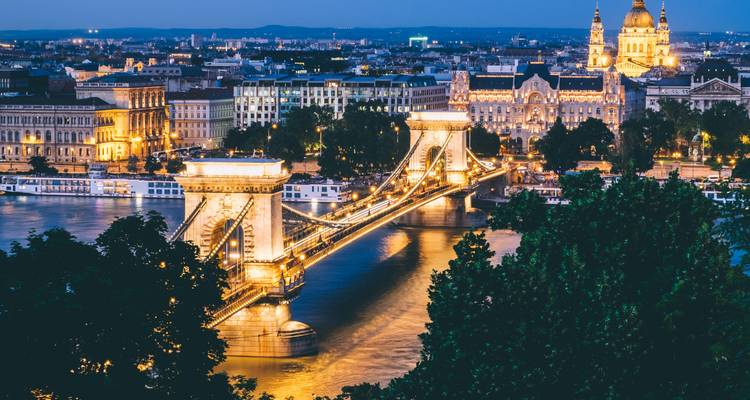 Budapest's illuminated Chain Bridge gleams over the Danube with St. Stephen's Basilica lit beyond.