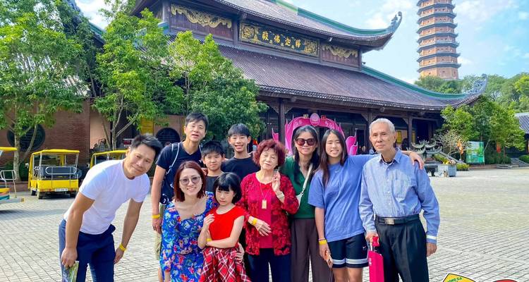 Grote familie die samen poseert voor een traditioneel Vietnamees pagondecomplex met een hoge stenen toren en weelderige bomen.