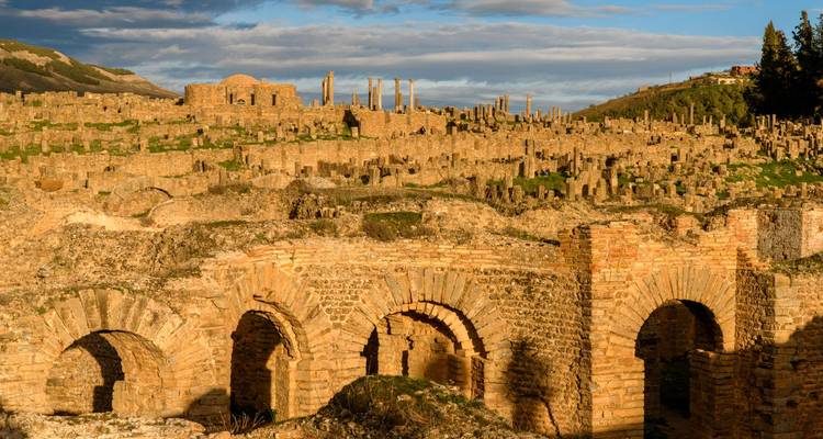 Uitgebreide Romeinse ruïnes met honderden stenen zuilen en bogen die glanzen in goudgeel licht.