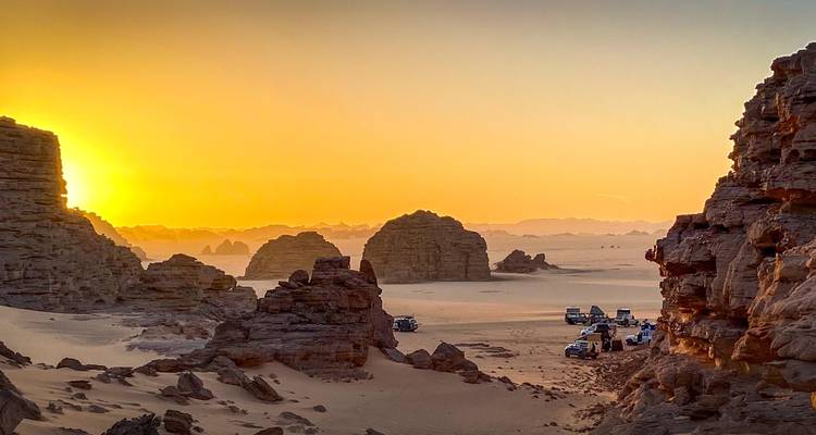 Zonsondergang verlicht 4x4-voertuigen die kronkelend door gesneden woestijnrotsen en duinen rijden.