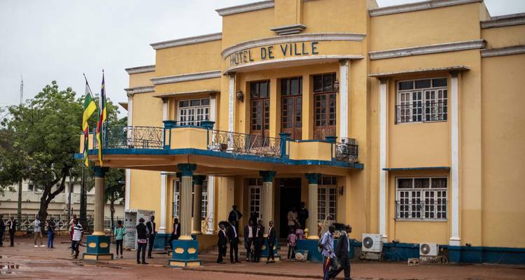 Yellow colonial-era city hall building with people gathered at the entrance on a wet street.