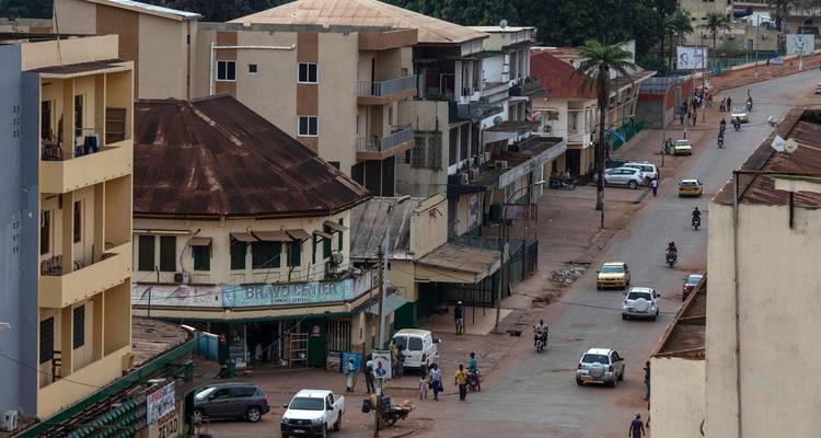 Aerial view of a busy main street with cars, motorbikes and low-rise buildings in a tropical city.