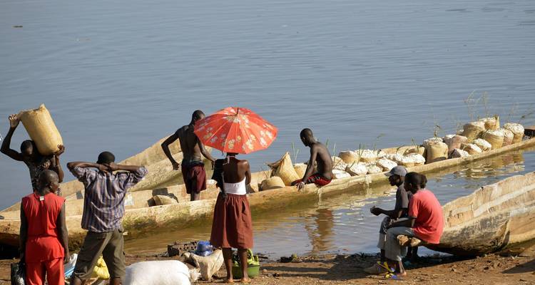 Local people loading goods into wooden dugout canoes on a riverbank.