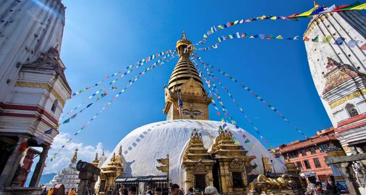 White stupa of Swayambhunath with golden spire and colourful prayer flags against clear sky.