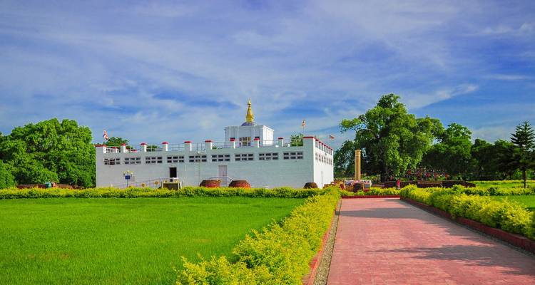 Maya Devi Temple in Lumbini surrounded by green lawns and a red brick path under blue sky.