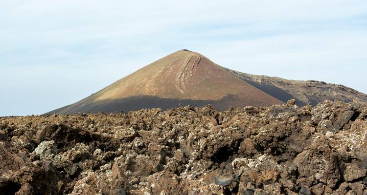 Kegelförmiger Vulkankegel, der sich über einem rauen Lavafeld erhebt