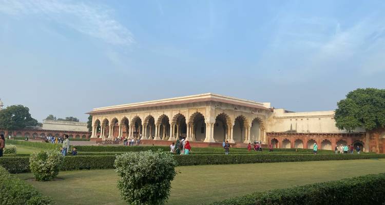 Bezoekers die door de gewelfde zuilengang van een Mughal-paleis binnenplaats wandelen, omgeven door verzorgde gazons.