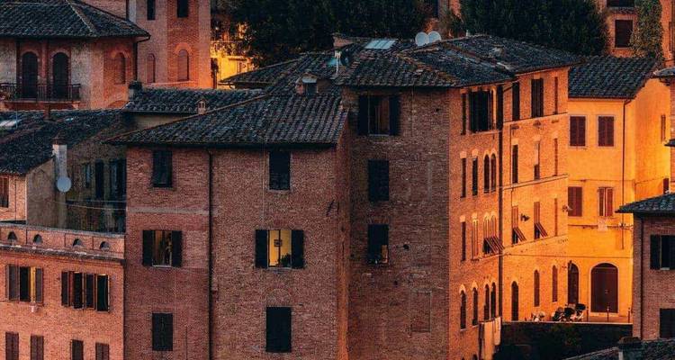 Sunset light bathes historic brick buildings with shuttered windows in a Tuscan hill town.