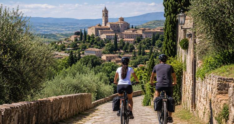 Two cyclists overlook a classic Umbrian hilltop village surrounded by rolling green countryside.