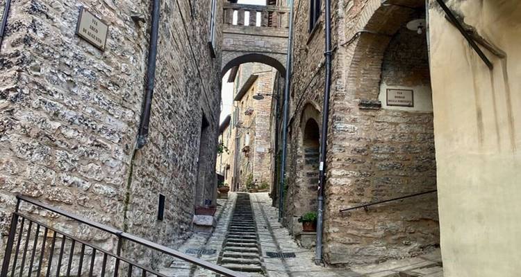Steep narrow staircase alley framed by stone walls and an arched bridge in an old town.