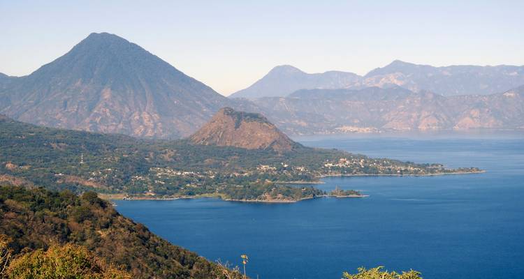 Wide view over deep blue Lake Atitlán encircled by volcanic peaks and forested hills.