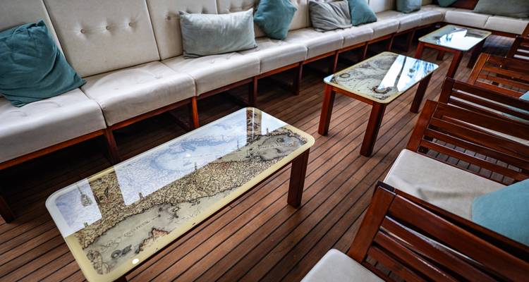 Detalle del área de asientos con mesas de cristal impresas con mapas náuticos vintage.
