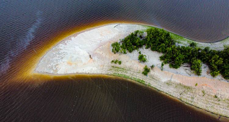 Toma aérea de una isla fluvial arenosa y cubierta de árboles rodeada por agua oscura.