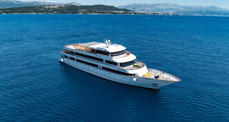 Elegant small cruise ship Adriatica sailing on calm Adriatic waters near a mountainous coastline.