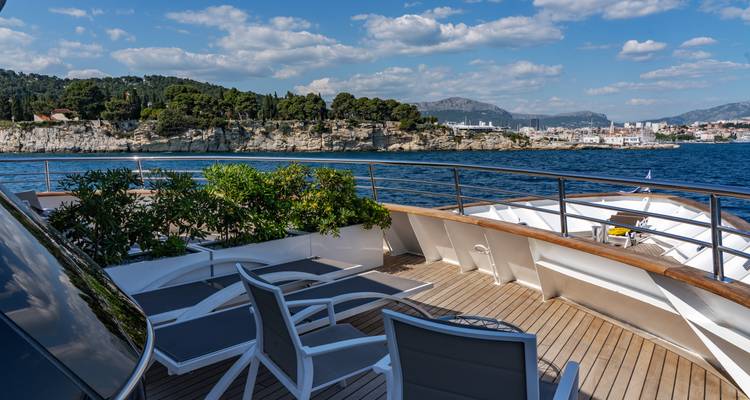 Bow lounging area with chairs overlooking a coastal city and cliffs.