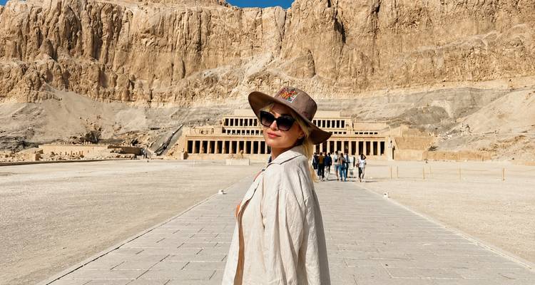 A stylish visitor stands before the grand Temple of Hatshepsut carved into towering cliffs.