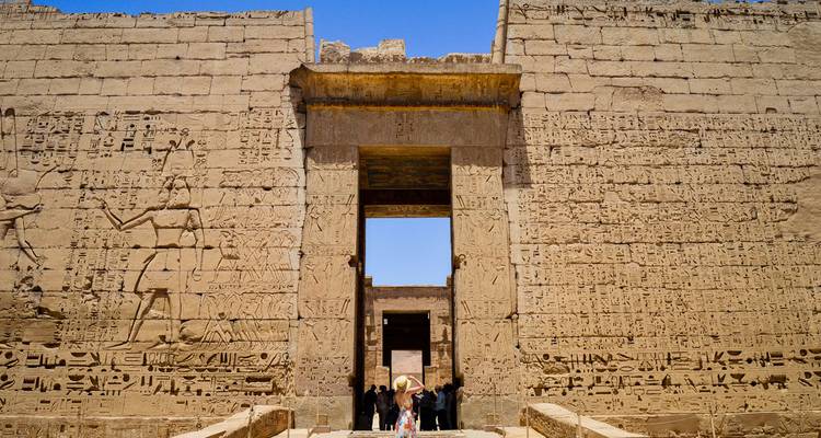 Visitors walk through a towering stone gateway densely covered with hieroglyphs.