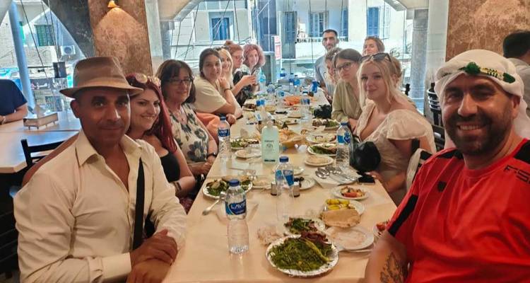 Large tour group enjoys a meal together at a long restaurant table filled with Middle Eastern dishes.