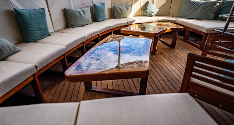 Outdoor lounge corner with cushioned bench seating and epoxy resin coffee tables on a teak deck.