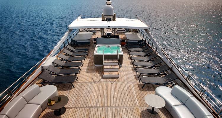 Spacious teak sundeck of a luxury yacht features loungers and a central jacuzzi.