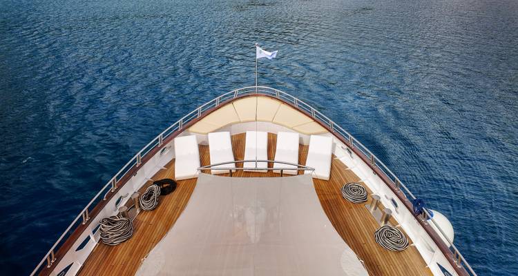 Bow view over yacht’s canvas sunbed toward open blue sea and clear sky.