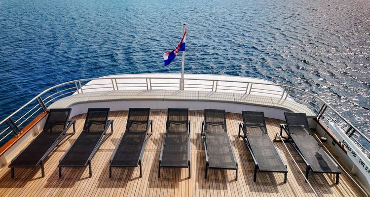 Row of sun loungers faces the sea on a yacht’s stern deck beneath the Croatian flag.