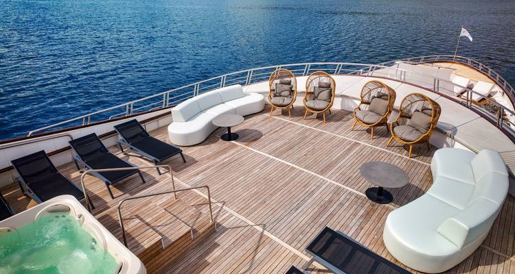 Spacious yacht sundeck with curved white sofas, loungers, hot tub and view of calm blue sea.