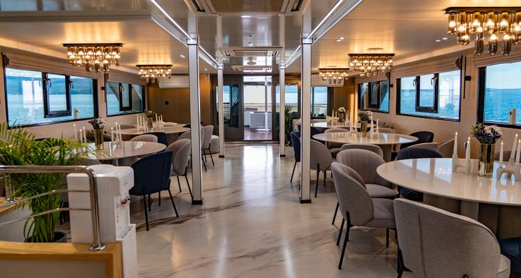 Elegant yacht dining salon with round tables, panoramic windows and marble floor.