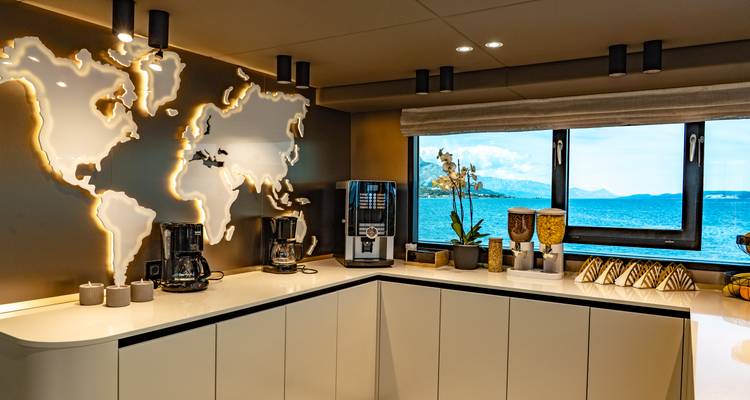 Bright yacht refreshment corner with illuminated world map, coffee machines and sea backdrop.