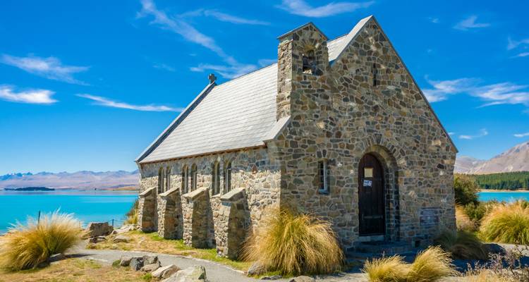 Stone Church of the Good Shepherd beside turquoise Lake Tekapo under clear blue skies.