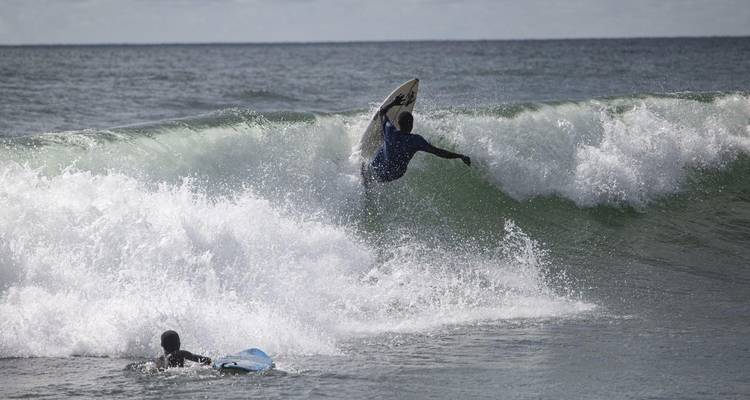 Surfer riding a breaking wave while another waits in the water.