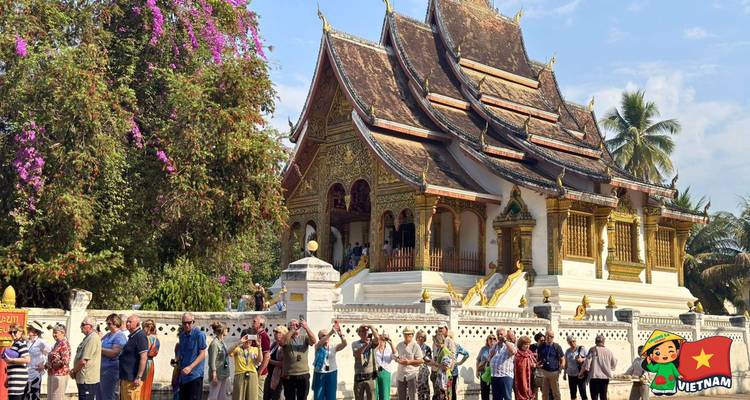 Tour group gathers outside an ornate golden Buddhist temple under a bright sky.