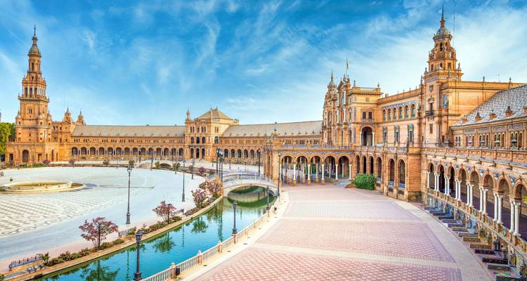 Panoramic sweep of the grand semicircular Plaza de España with canal, bridges and soaring towers under a vivid sky.